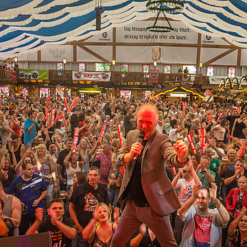 De Beierse feesttent bij de Cranger Kirmes is tot de nok toe gevuld met gasten: de presentator kijkt enthousiast in de camera.