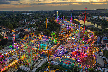 Een foto van de Cranger Kirmes na zonsondergang: je ziet veel verlichte carrousels, kermiswinkels en mensen.