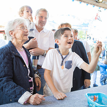 Een kind speelt darts bij de Cranger Kirmes en wordt vergezeld door oma, broers en zussen en ouders. 
