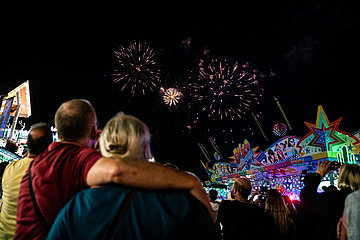 Het legendarische vuurwerk bij de Cranger Kirmes. Ervoor zie je mensen op de kermis naar het spektakel in de lucht kijken. Links en rechts zijn kermisattracties te zien.