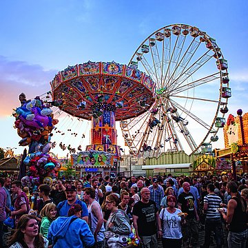 Een foto van de Cranger Kirmes: je ziet kettingcarrousels, veel mensen en een reuzenrad.